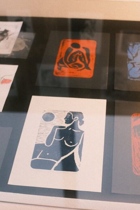 Kilka oprawionych grafik przedstawiających figuratywne i botaniczne ilustracje w stylu drzeworytu, wyeksponowanych pod szkłem.